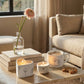Candlelit coffee table with candles, a mug, cookies, and a vase with a flower in a cozy living room.